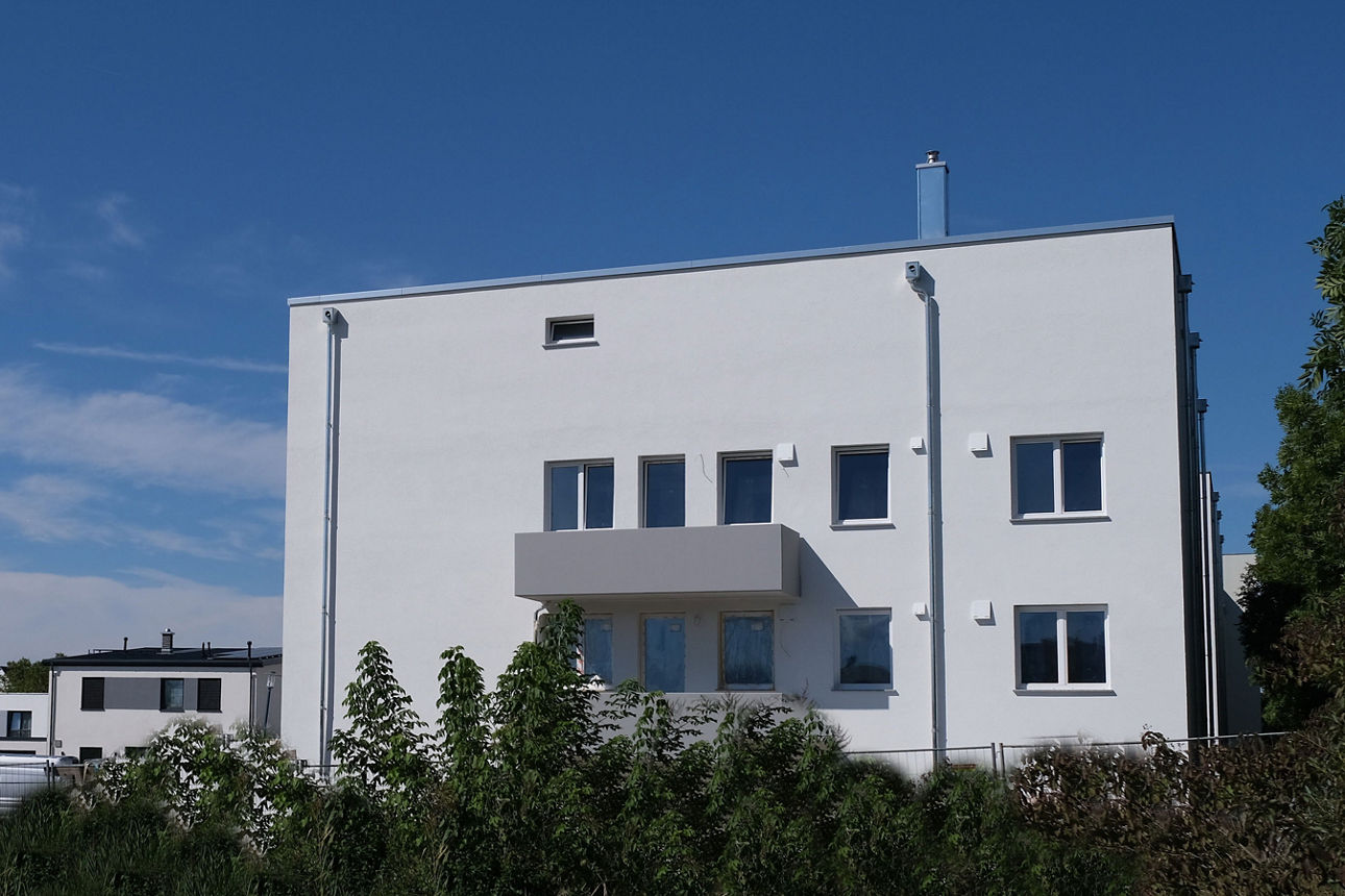Moderne Wohnanlage mit Mehrfamilienhäusern, Balkonen und parkendem Auto in ruhiger Wohnstraße.