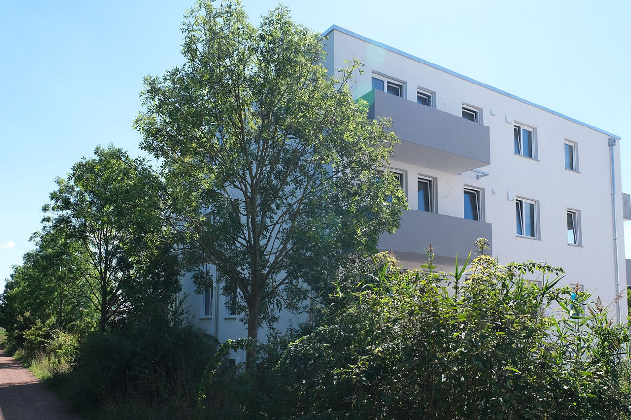 Moderne Wohnanlage mit Mehrfamilienhäusern, Balkonen und parkendem Auto in ruhiger Wohnstraße.