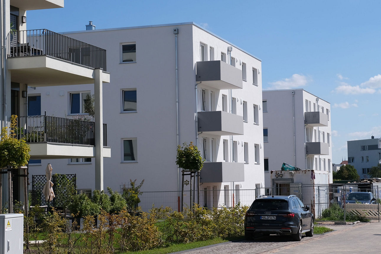Moderne Wohnanlage mit Mehrfamilienhäusern, Balkonen und parkendem Auto in ruhiger Wohnstraße.
