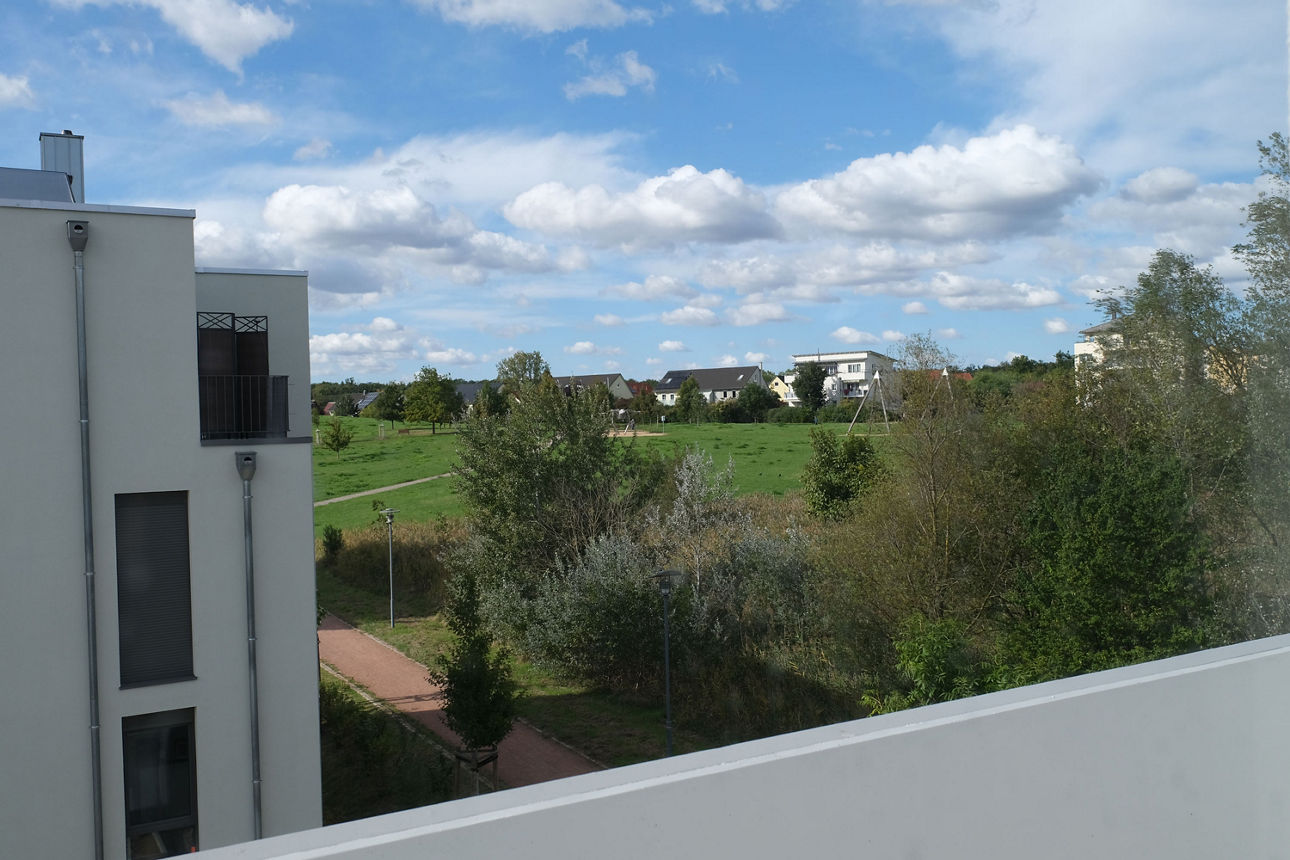 Moderne Wohnanlage mit Mehrfamilienhäusern, Balkonen und parkendem Auto in ruhiger Wohnstraße.