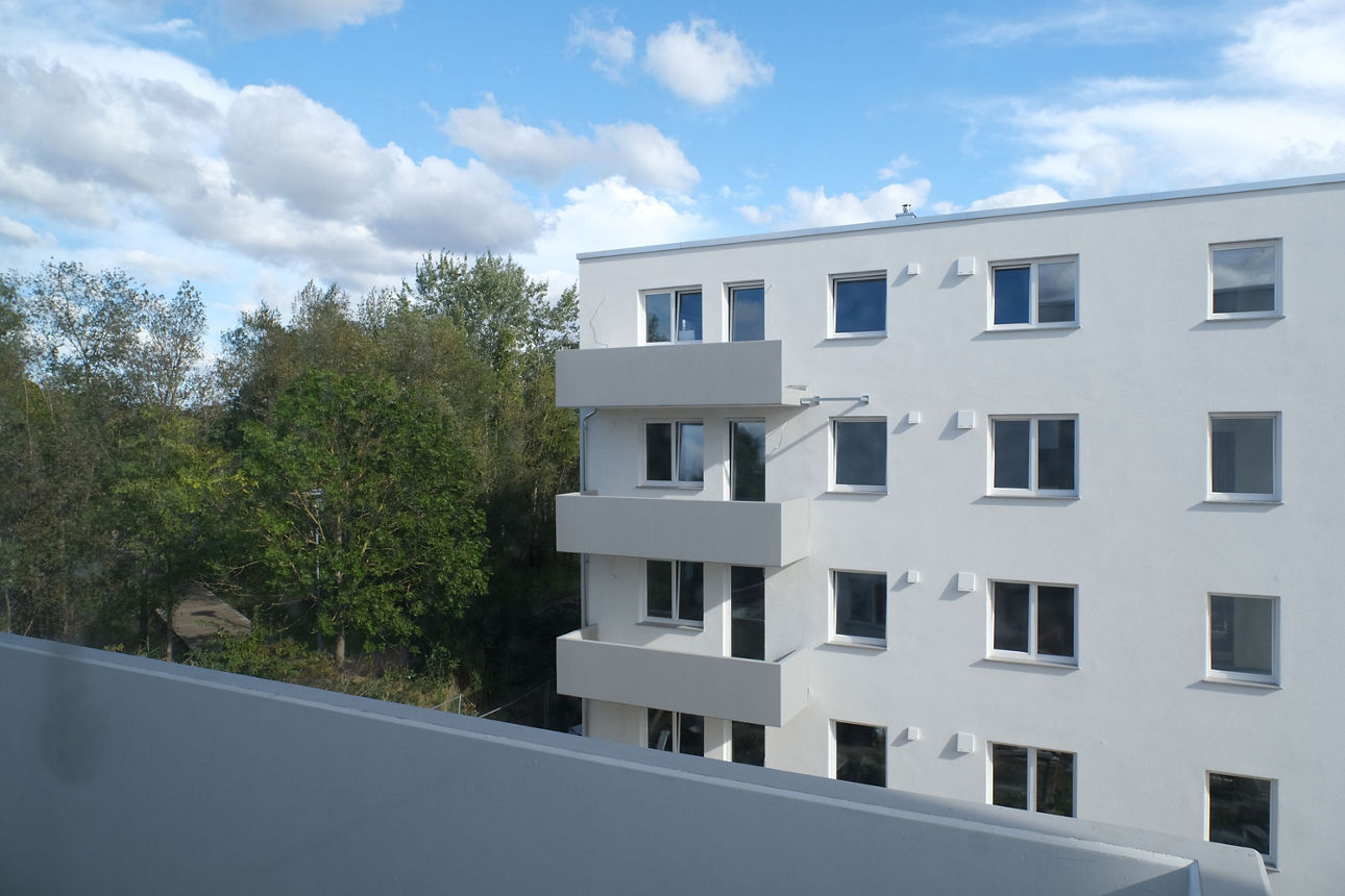 Moderne Wohnanlage mit Mehrfamilienhäusern, Balkonen und parkendem Auto in ruhiger Wohnstraße.