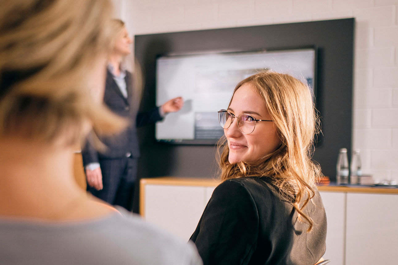 Zwei lächelnde Frauen sitzen nebeneinander in einem Büro