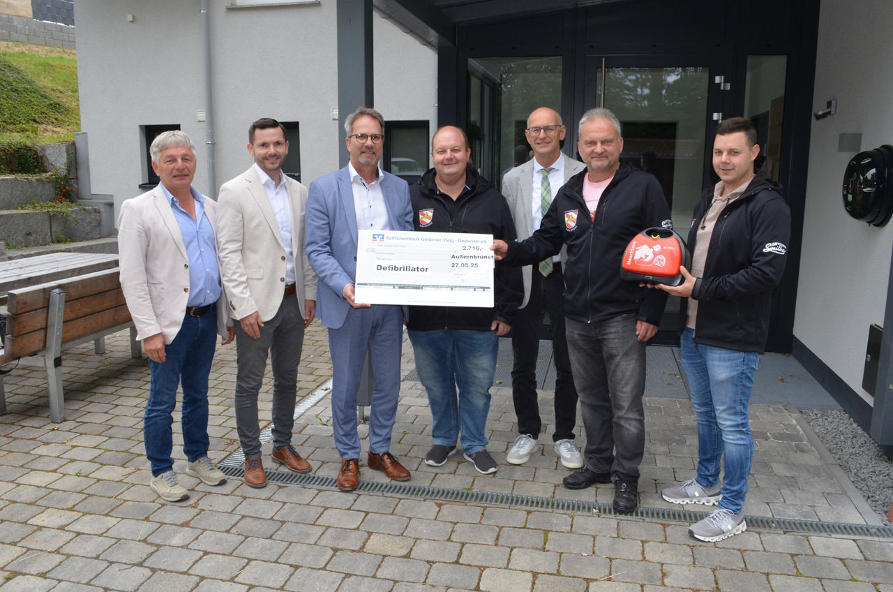 4 Herren halten einen Scheck in der Hand und einen roten Defibrilator