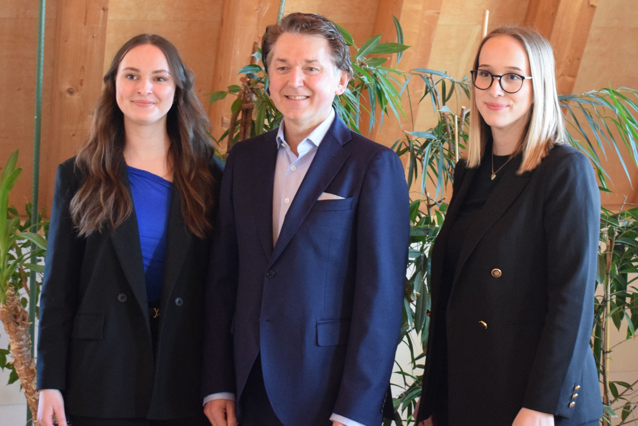 Ein Mann und zwei junge Frauen in Anzügen posieren für ein Foto