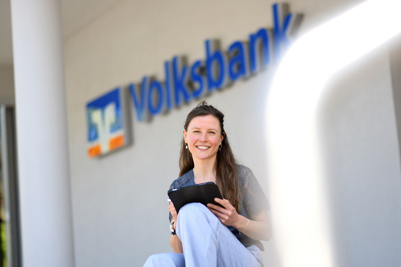 Mitarbeiterin der Volksbank sitzt mit Tablet lächelnd auf Stufe