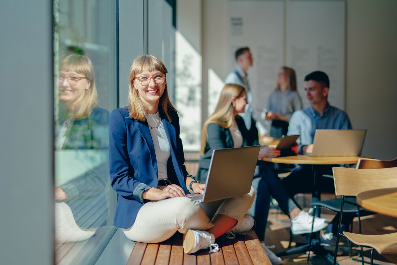 Studentin lehnt mit Laptop am Fenster