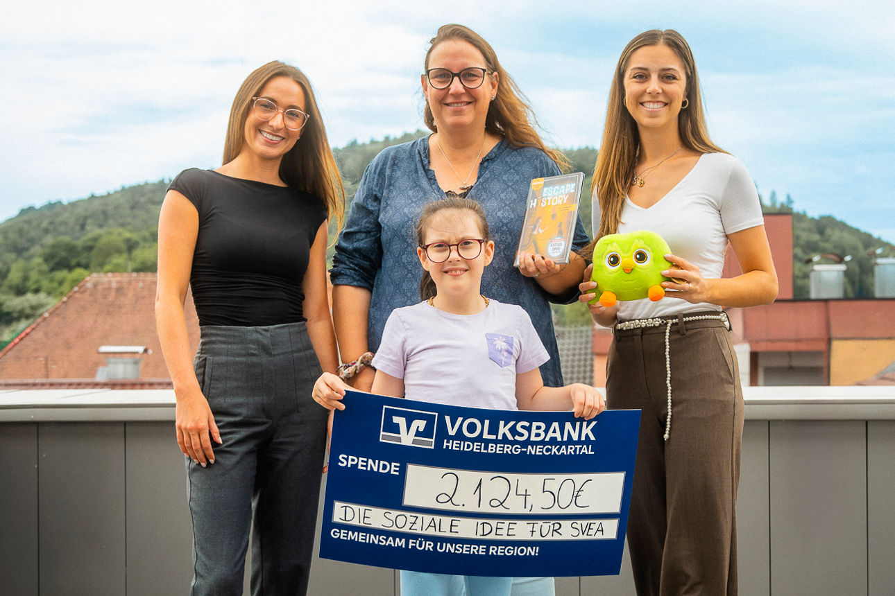 Personen stehen auf einer Dachterasse und übergeben an Svea einen Scheck