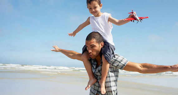 Mann trägt einen Jungen auf den Schultern am Strand