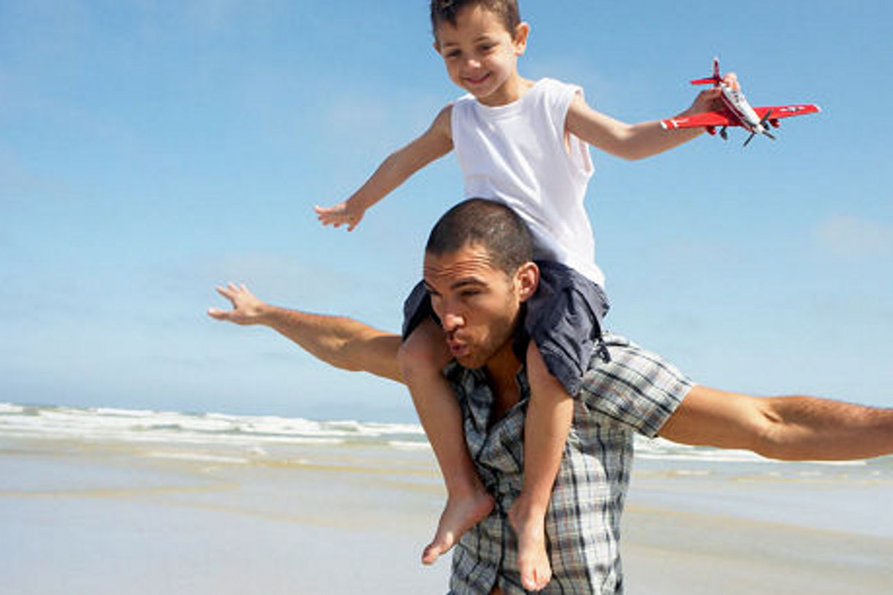 Mann trägt einen Jungen auf den Schultern am Strand