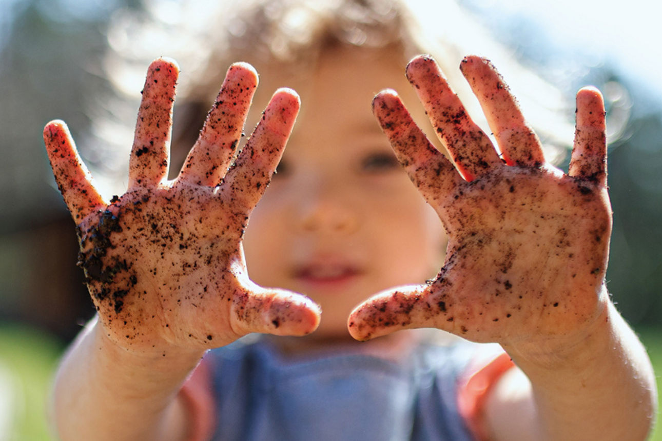 Ein kleines Mädchen hält ihre mit Erde bedeckten Hände nach vorne.
