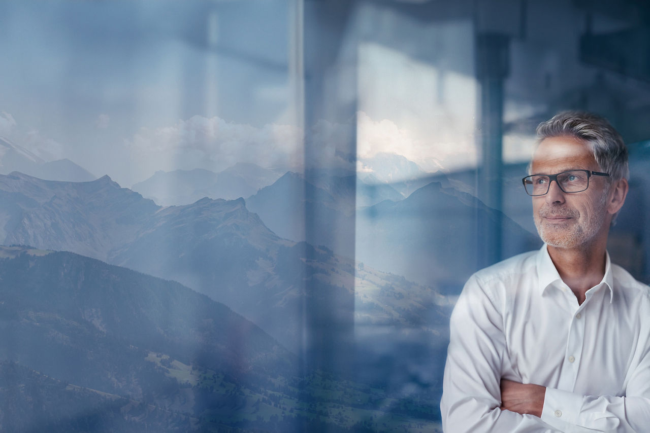 Ein Mann lehnt an einem Fenster, im Hintergund kann man Berge erkennen.