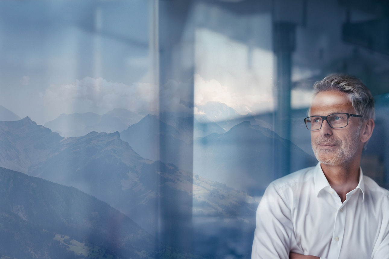 Ein Mann lehnt an einem Fenster, im Hintergund kann man Berge erkennen.