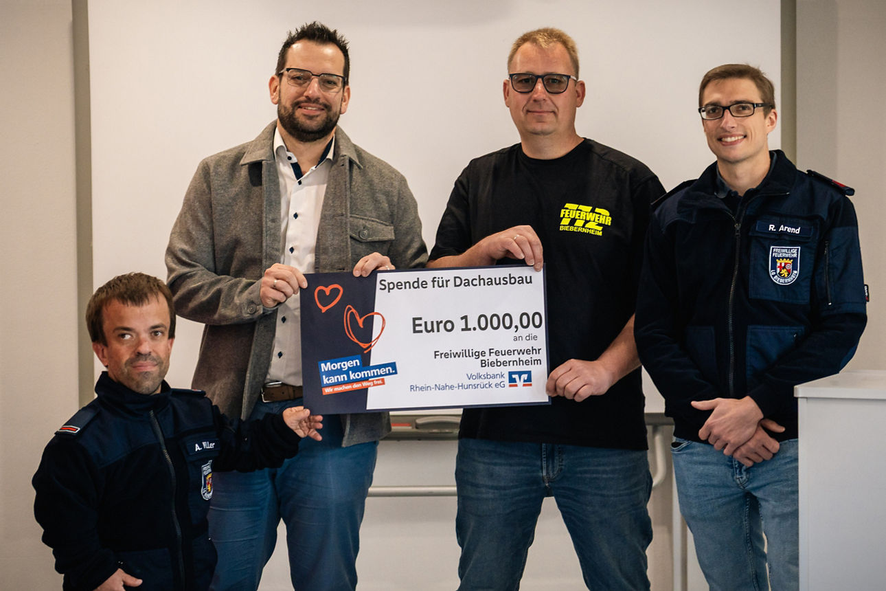 Vier Erwachsene halten einen Spendenscheck in der Hand. 