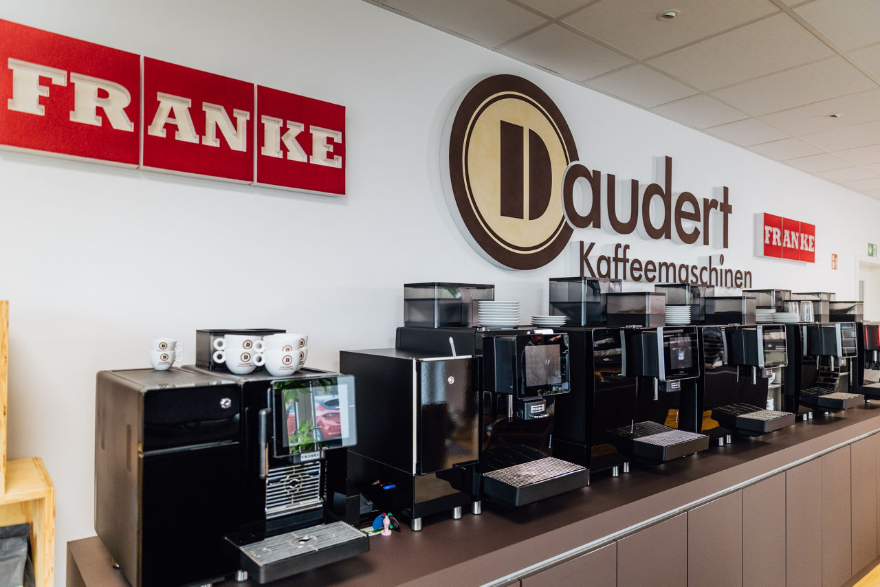 Innenaufnahme Daudert mit mehreren professionellen Kaffeemaschinen und Kaffeemühlen, im Vordergrund steht eine Person vor einer Espressomaschine