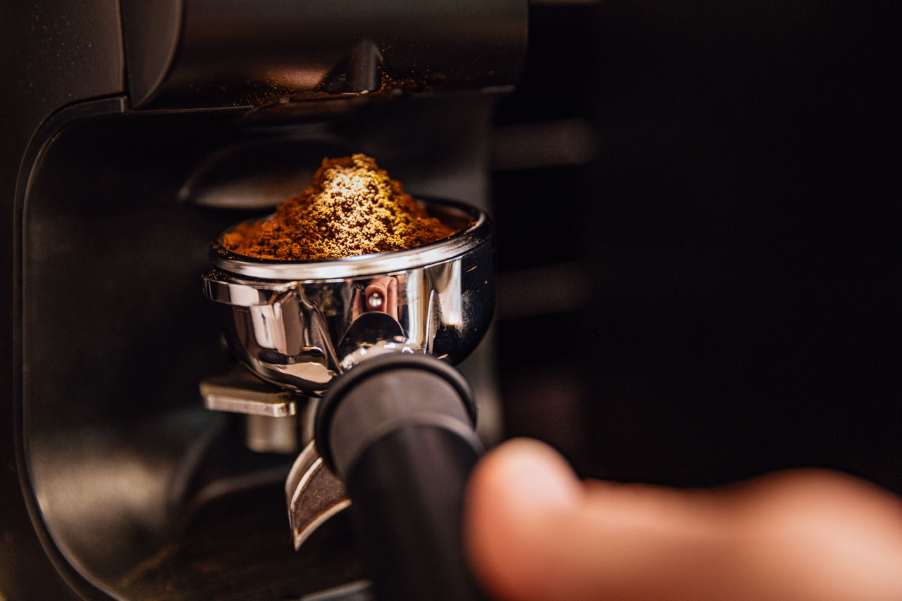 Detailaufnahme einer Kaffeemühle mit eingespanntem Siebträger und frisch gemahlenem Kaffeepulver.