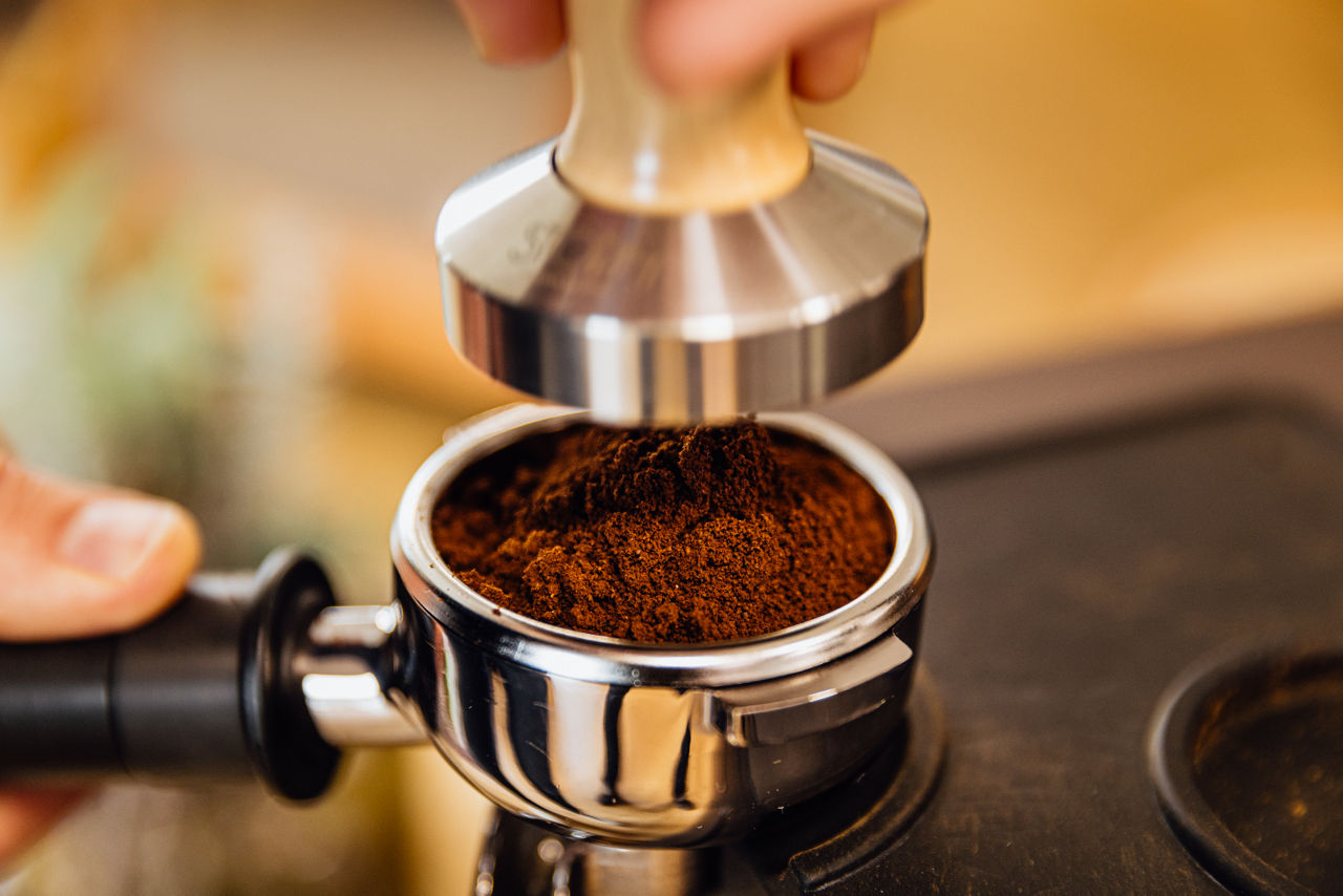 Detailaufnahme eines Siebträgers mit frisch gemahlenem Kaffeepulver während der Vorbereitung für die Kaffeezubereitung.