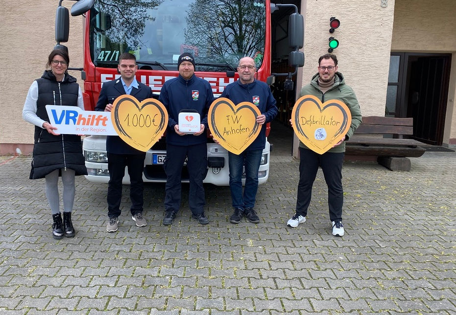 Fünf Menschen halten orangefarbene Herzen aus Pappe vor einem Feuerwehrauto