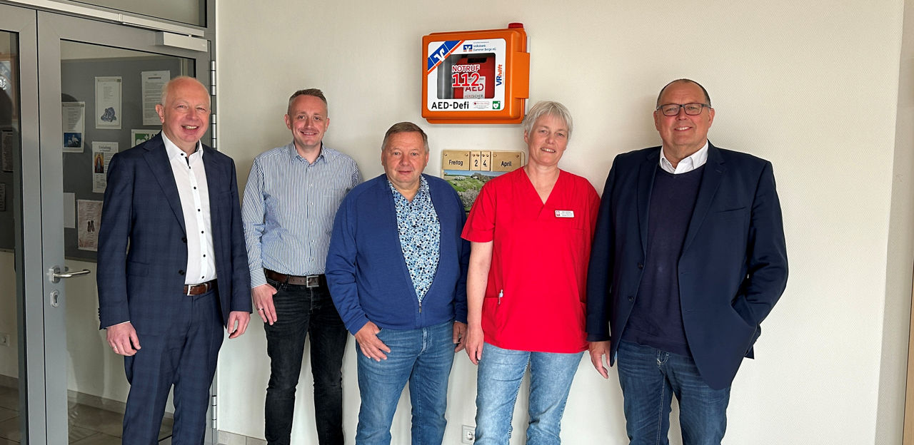 Vier Männer und eine Frau haben sich vor einem Defibrilator zum Foto aufgestellt. 