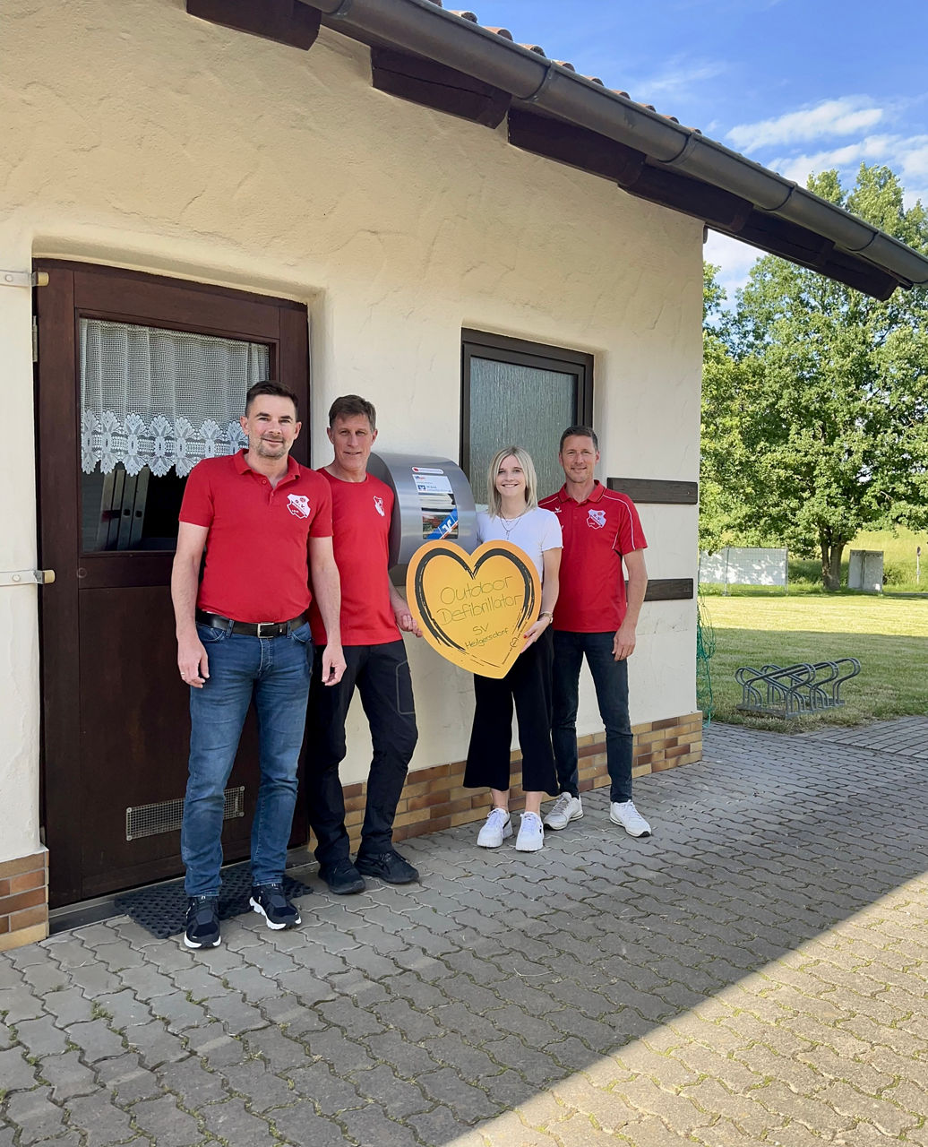 Kundenbetreuerin Sophie Werner übergibt den Defibrillator an Jens Hartmann, Udo Scharpf und Marco Schramm vom SV Heilgersdorf
