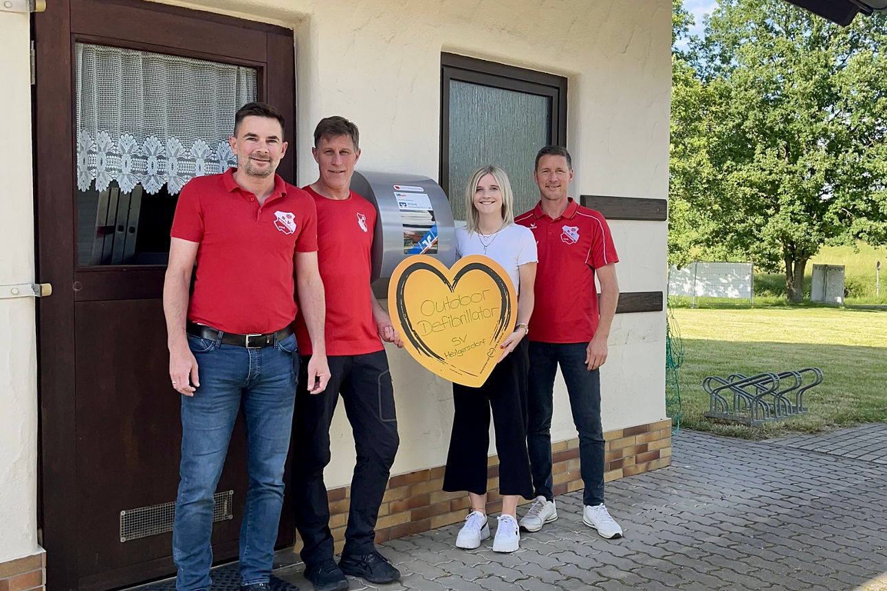 Kundenbetreuerin Sophie Werner übergibt den Defibrillator an Jens Hartmann, Udo Scharpf und Marco Schramm vom SV Heilgersdorf