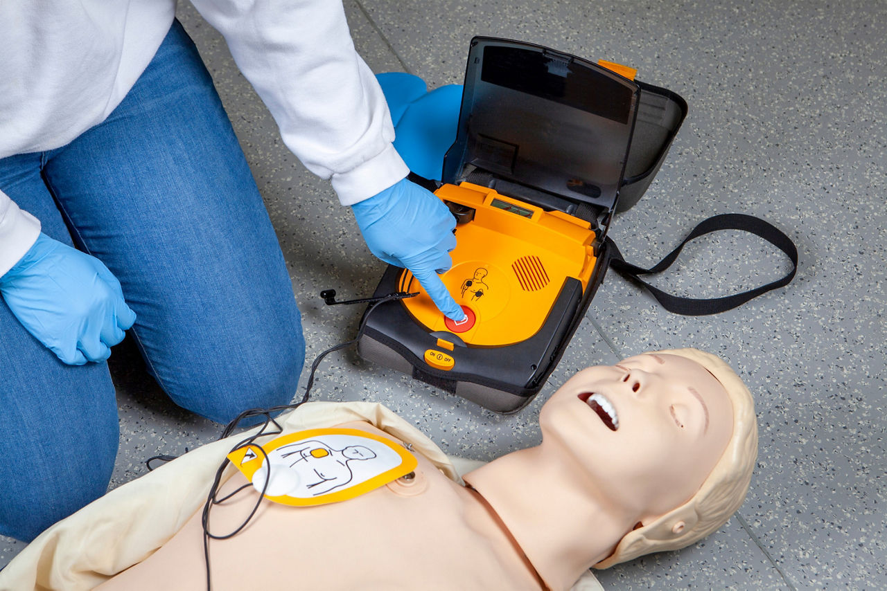 Defibrillator - Ersthelfer mit Übungspuppe demonstrieren die Benutzung eines Defibrillators