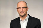 Dirk Demeuth hat eine Brille, ganz kurze Haare und einen Dreitagebart. Er trägt einen Anzug.