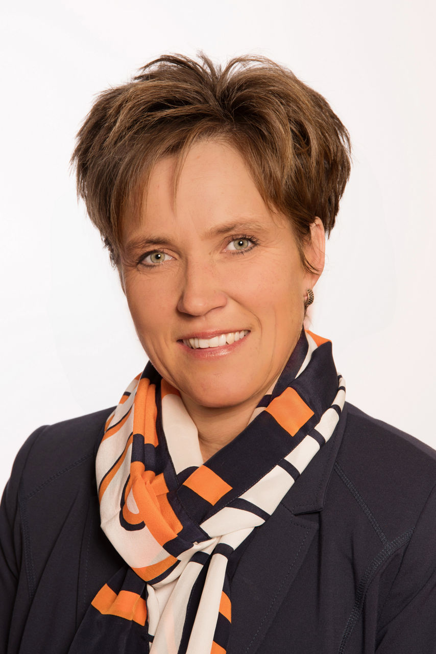 Petra Demmel, eine lächelnde Frau mit kurzen braunen Haaren, trägt einen Blazer und einen Schal mit orange-blauen und weißen Mustern.