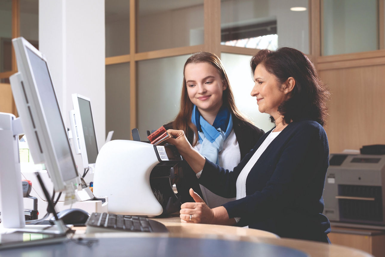 Zwei Mitarbeiterinnen stehen am Schalter und nutzen die Geldzählmaschine