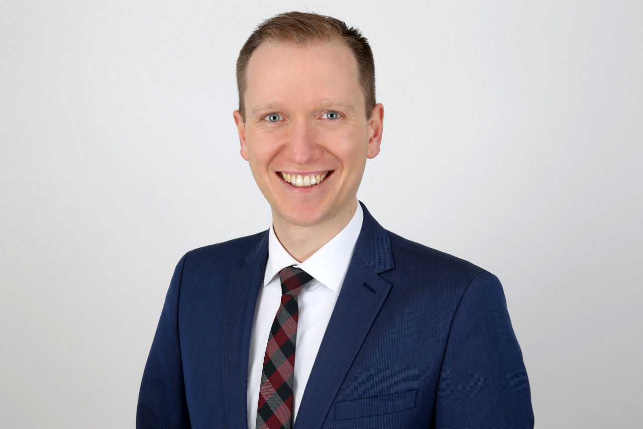 Ein lächelnder Mann in einem Anzug schaut in die Kamera.