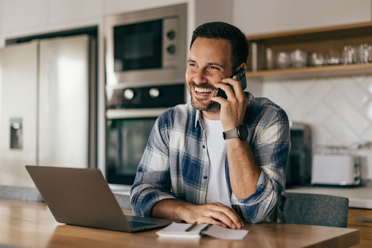ein lächelnder Mann sitzt zu Hause vor dem Laptop und telefoniert