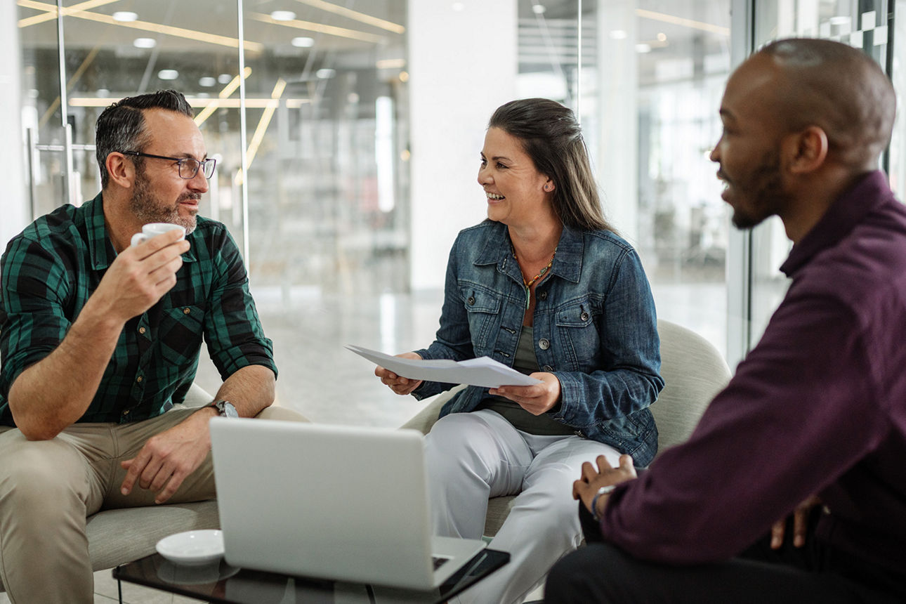 drei Personen sitzen zusammen vor einem Laptop und reden