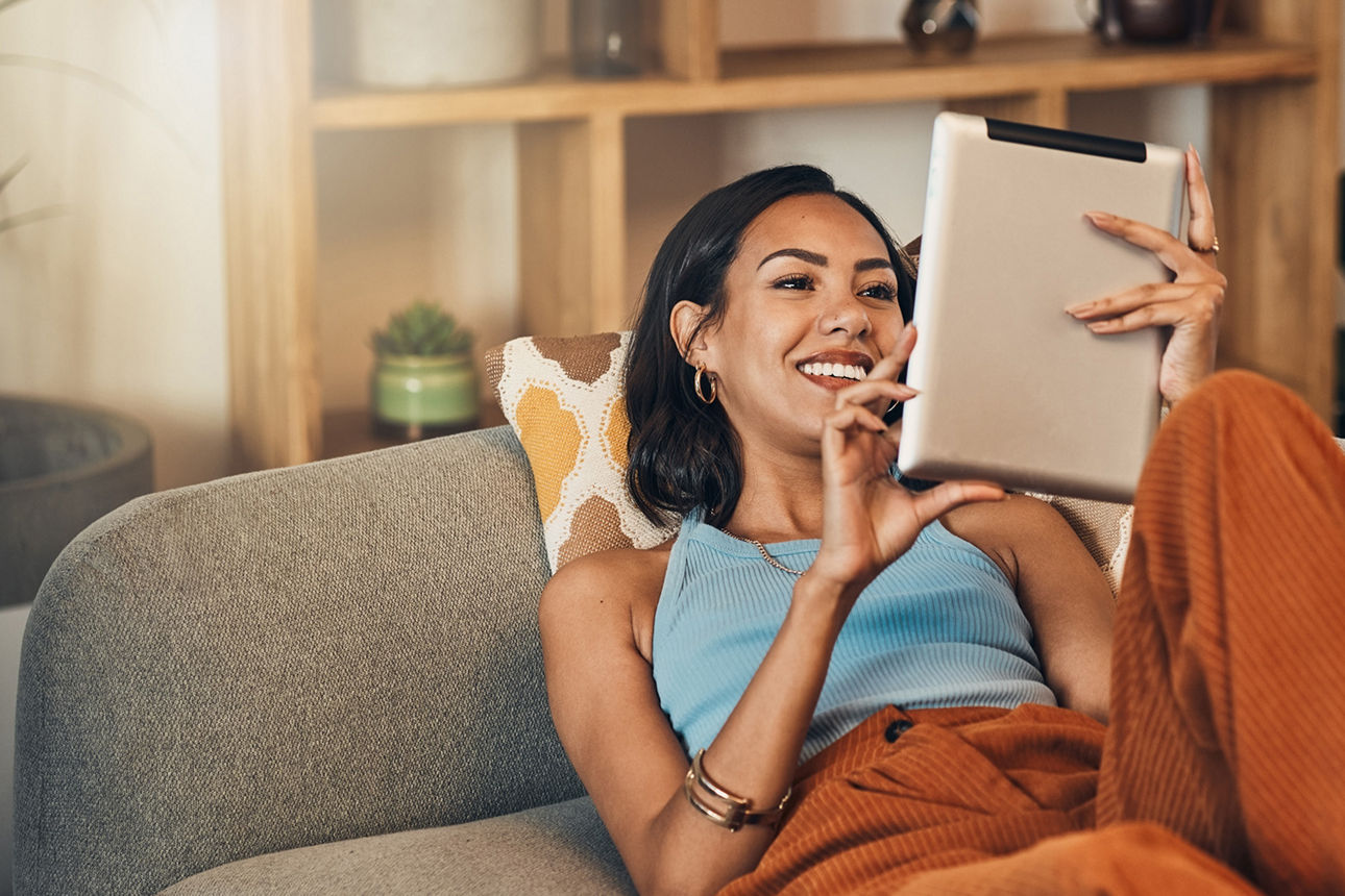 eine junge Frau liegt auf dem Sofa und schaut auf Ihr Tablet