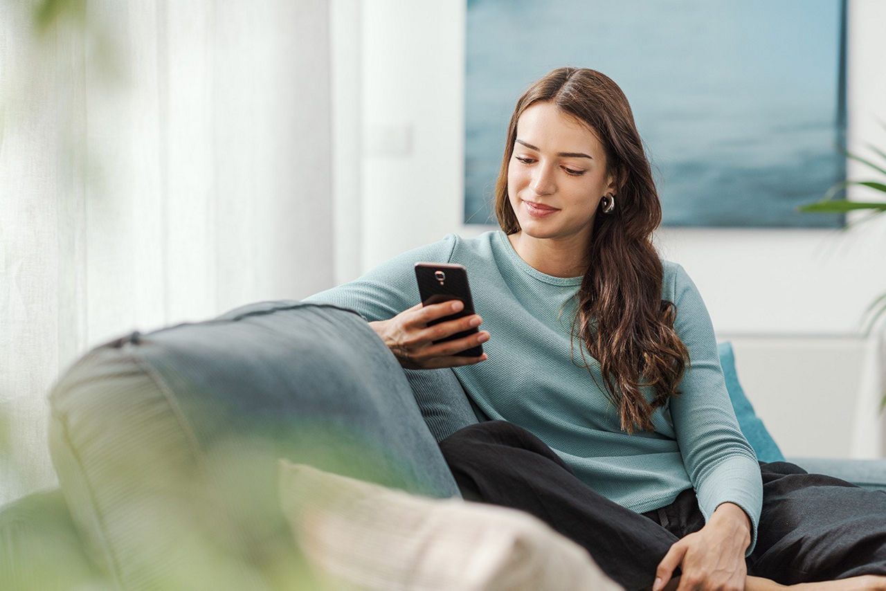 Frau sitzt mit ihrem Handy auf dem Sofa