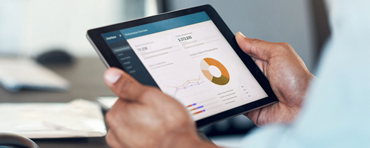 zwei Hände halten ein Tablet vor einem Schreibtisch
