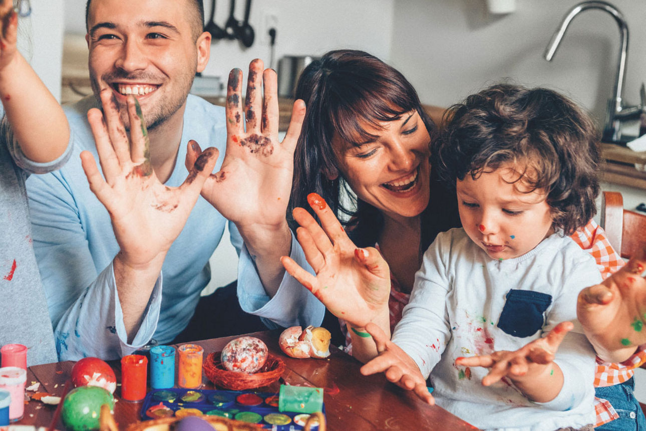 Familie bemalt gemeinsam Ostereier am Tisch und hat dabei sichtlich Spaß.