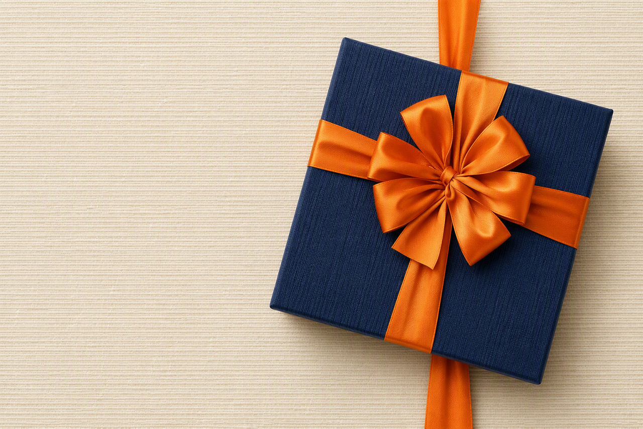 Geschenk im dunkelblauen Papier mit einer orangenen Schleife auf beigen Hintergrund.