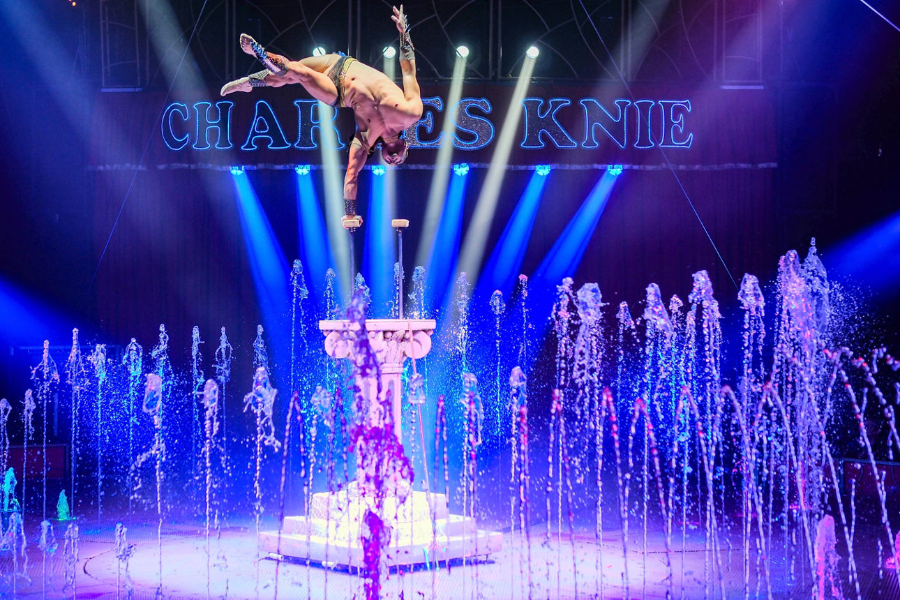Spektakuläre Artistik in der Wassershow SPLASH des Zirkus Charles Knie: Akrobat auf Handstäben vor beleuchteten Wasserfontäne