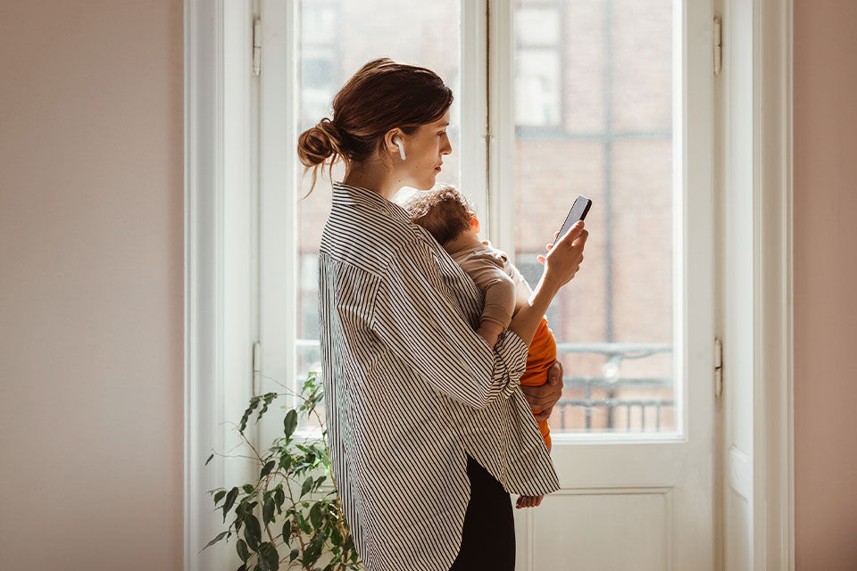 Frau mit Baby im Arm telefoniert mit Smartphone