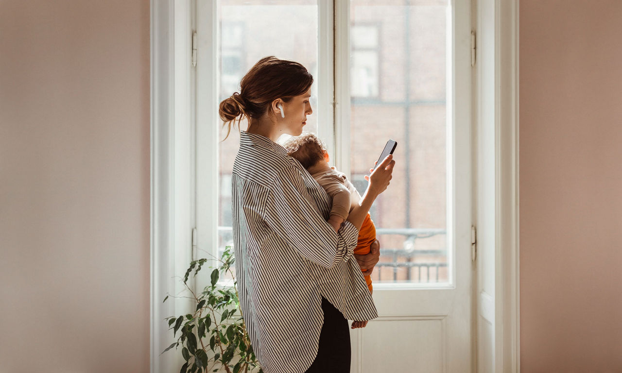 Frau mit Baby im Arm telefoniert mit Smartphone