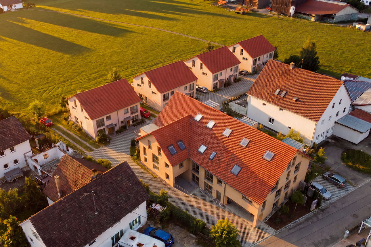 Rückansicht eines modernen, weißen Mehrfamilienhauses mit mehreren Balkonen, großem Garten und Solaranlage auf dem Dach unter