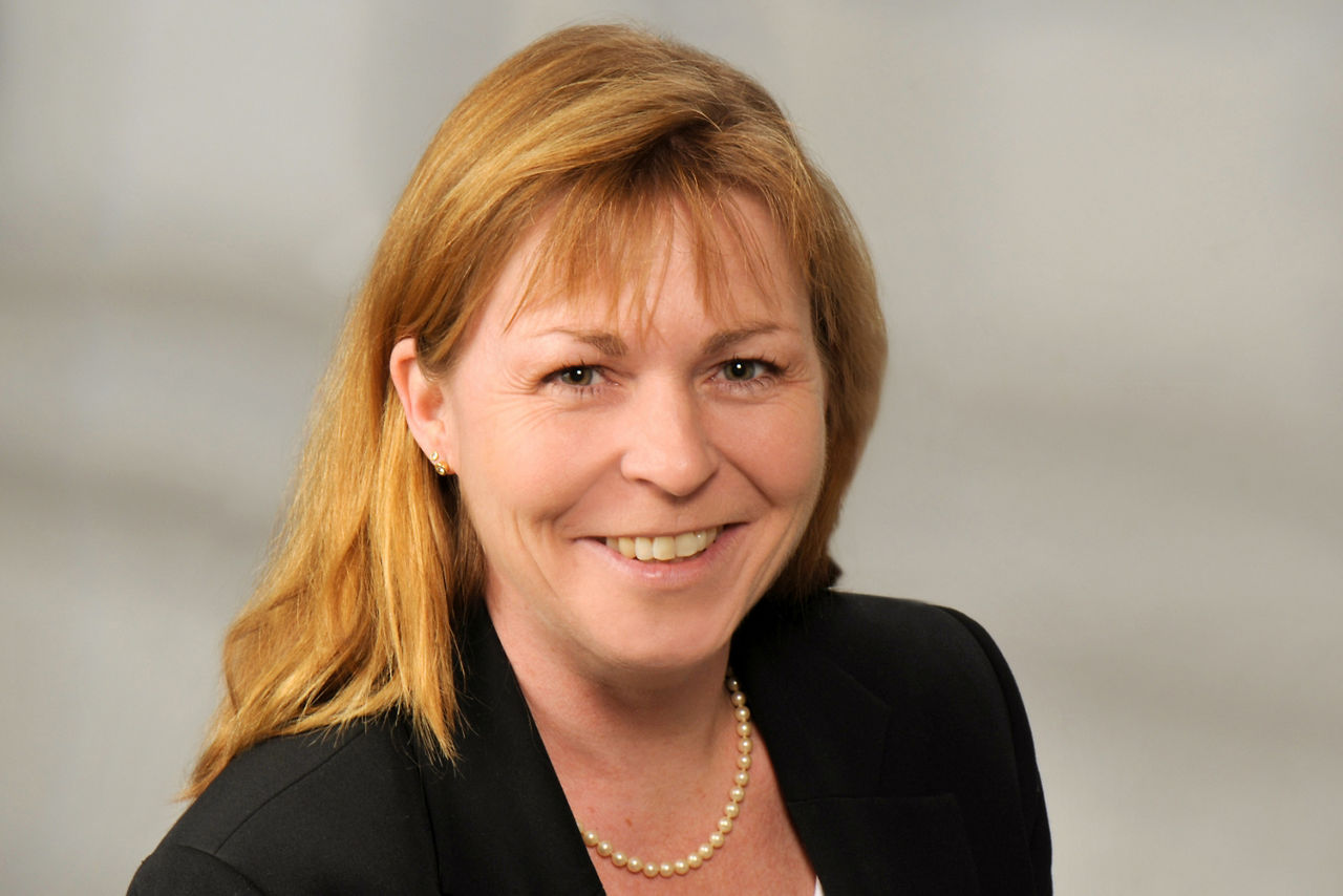 Daniela Diefenbach hat lange blonde Haare mit einem Pony, sie trägt eine Perlenkette und ein schwarzen Blazer