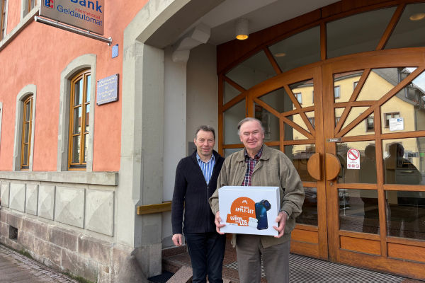 Zwei Männer stehen vor dem Eingang einer Bank. Der ältere Mann hält eine Box mit der Aufschrift "Apple-Set Gewinnsparlos.