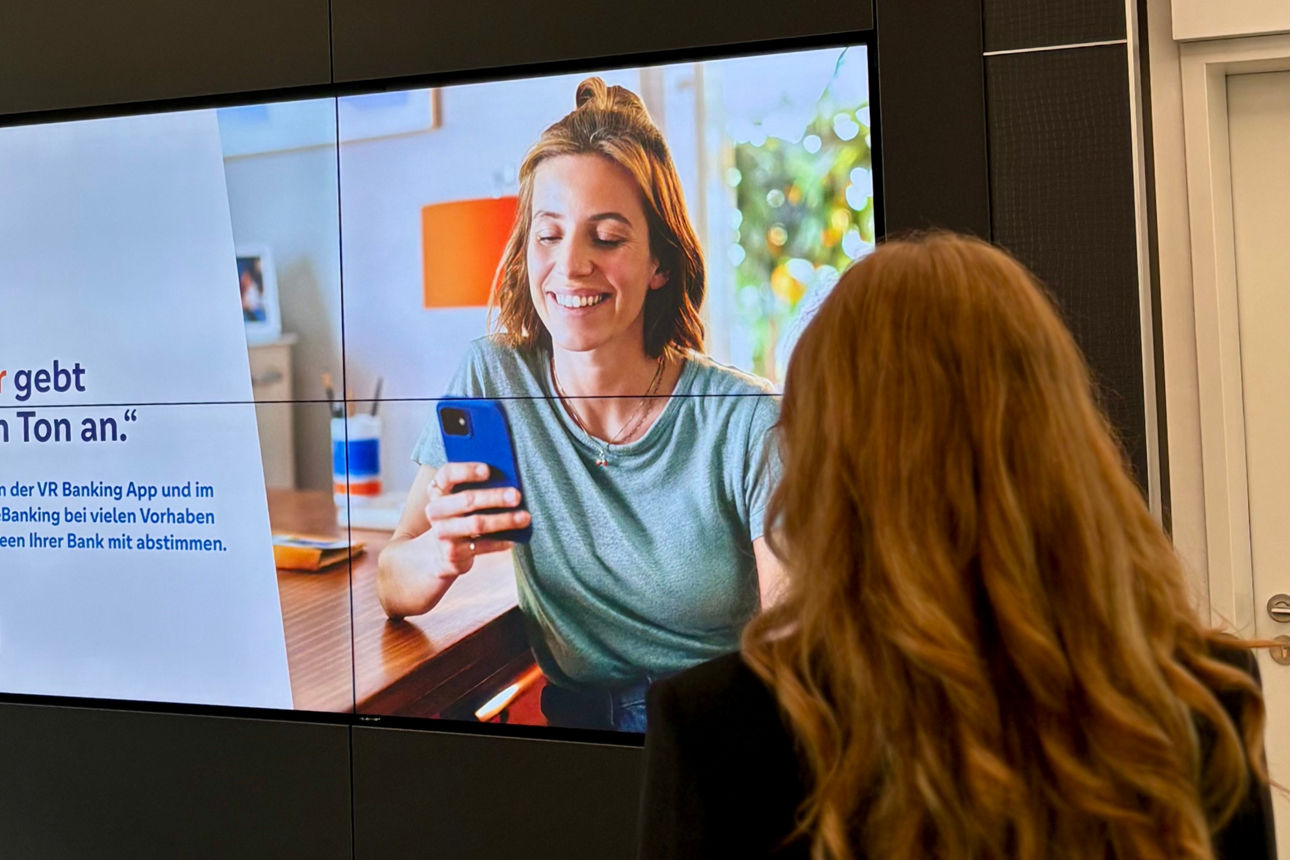 Eine Frau steht in unserer Hauptstelle mit dem Rücken zur Kamera vor unseren digitalen Werbeflächen.