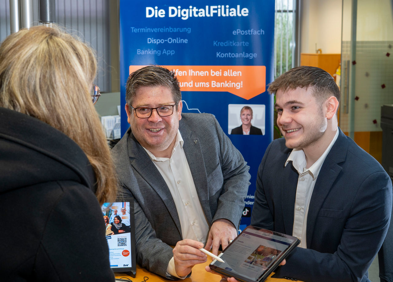 Kollegen der Digitalfiliale erklären einer Kundin in der Geschäftsstelle etwas am Tablet