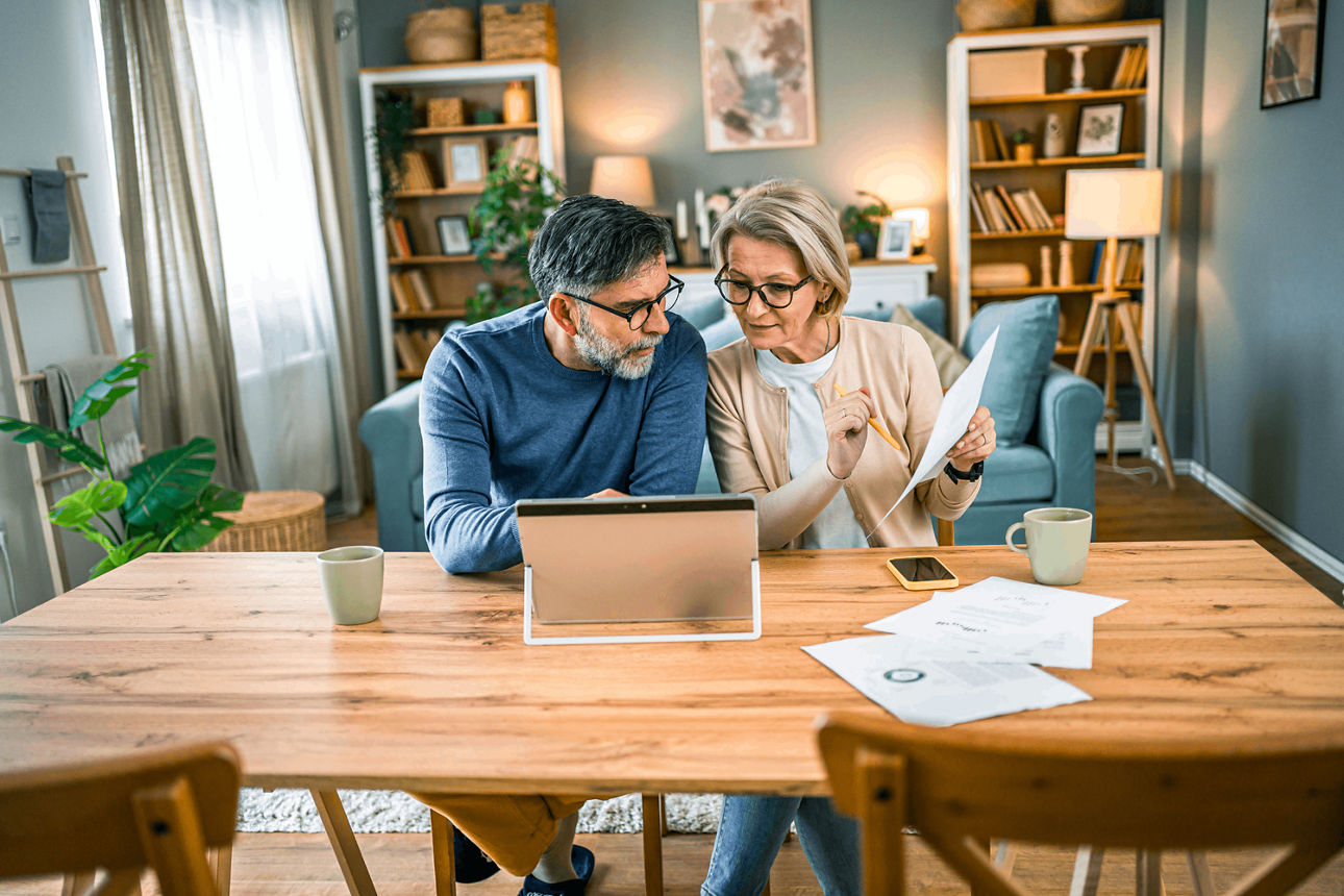 Ein Paar sitzt am Esstisch zu Hause, prüft Unterlagen und erledigt Bankgeschäfte digital zuhause.