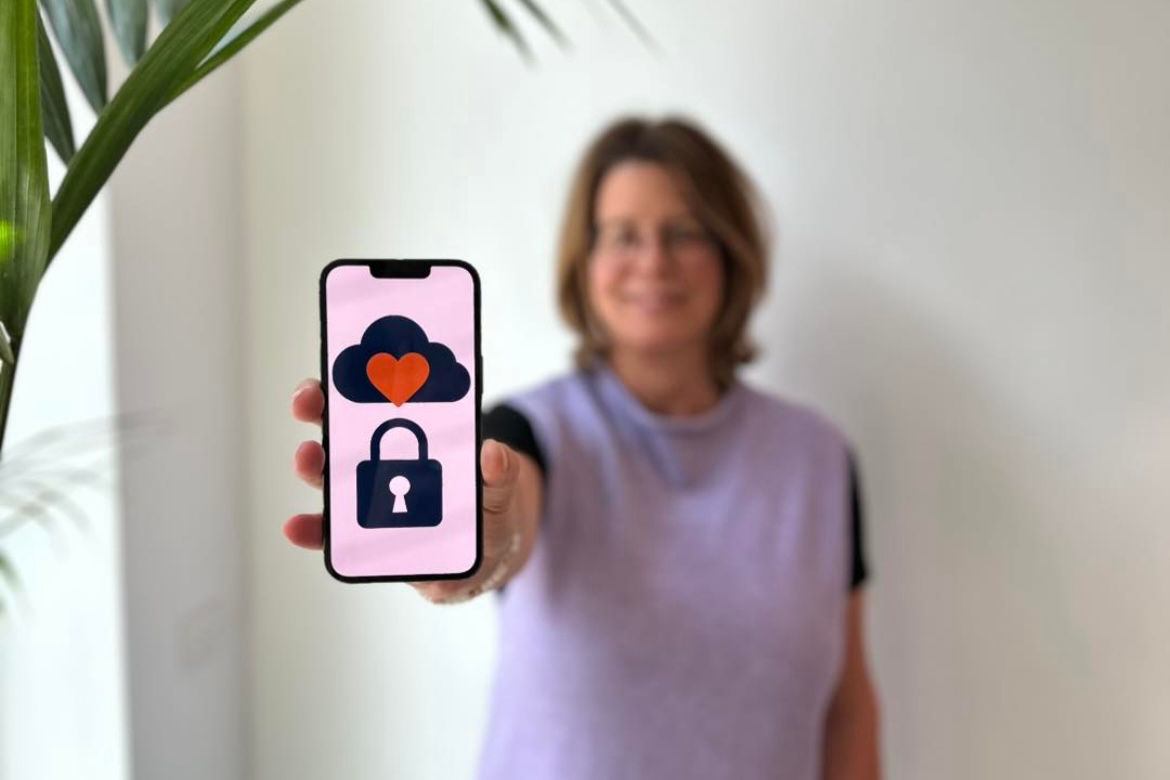 Ein Handy mit den Symbolen einer Wolke, eines roten Herzens und einem Schloss wird von einer Frau in die Kamera gehalten