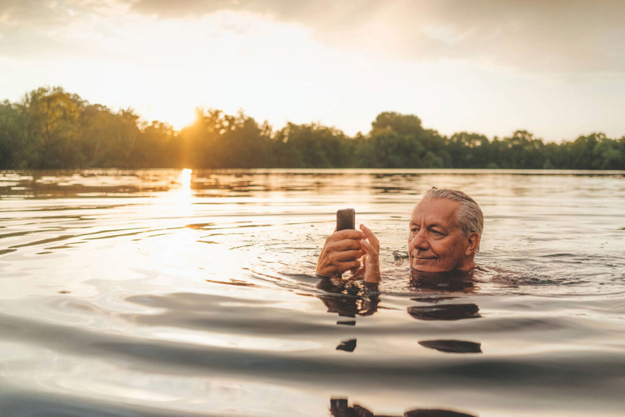 Ein Mann schwimmt mit seinem Smartphone im See.