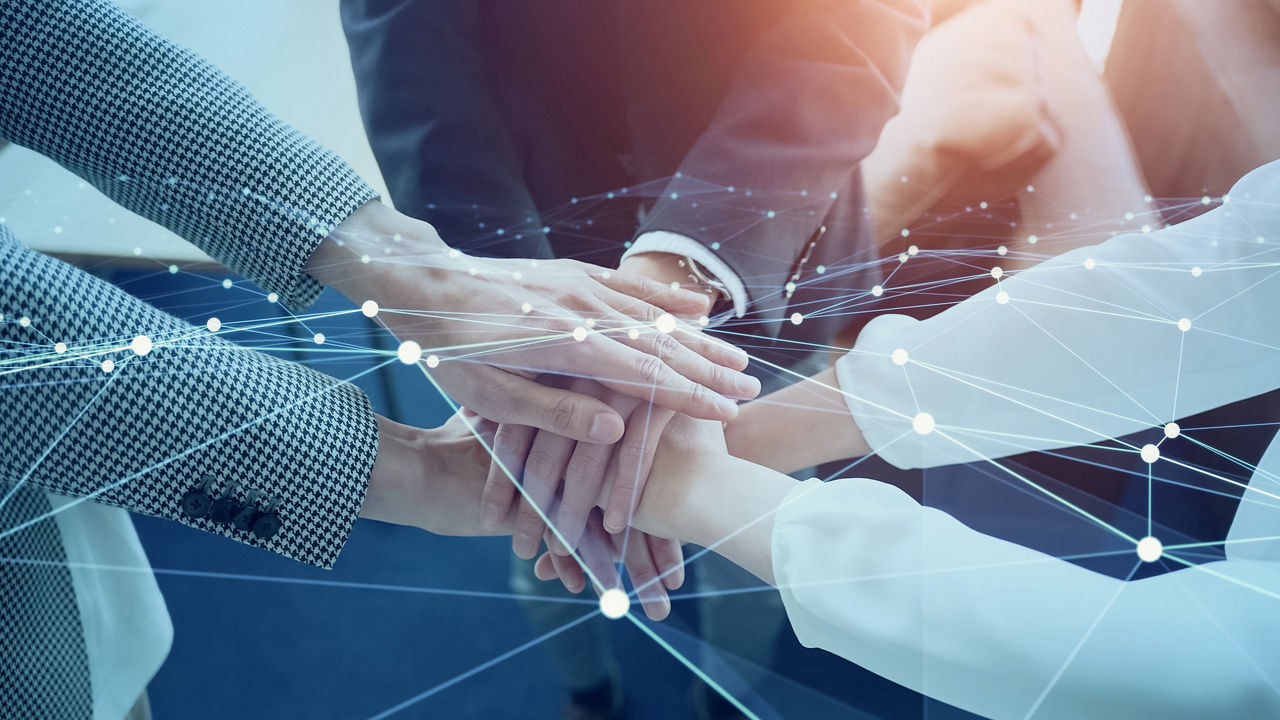 Mehrere Personen legen ihre Hände übereinander, symbolisch für Teamwork und digitale Vernetzung.