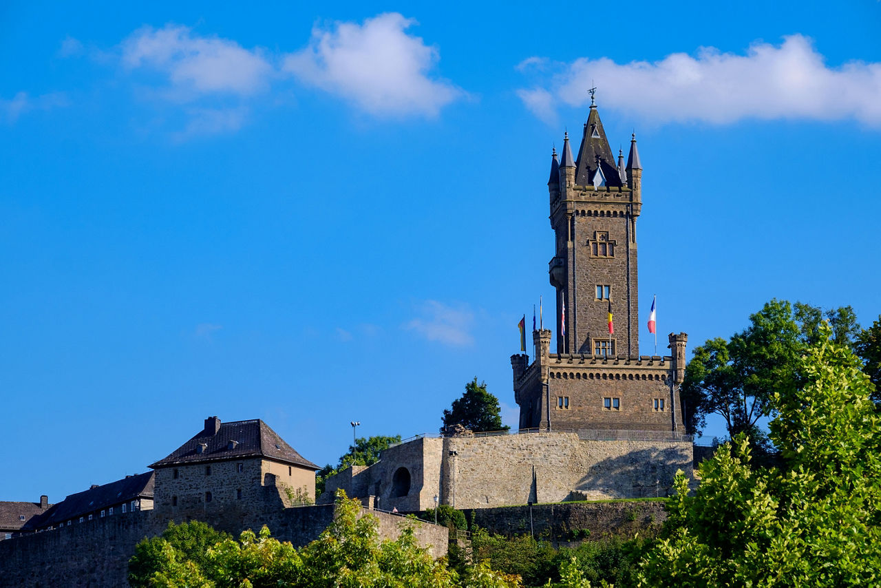 Der Wilhelmsturm in Dillenburg erhebt sich bei strahlend blauem Himmel über die umliegenden historischen Gebäude und ist mit mehreren Flaggen geschmückt.