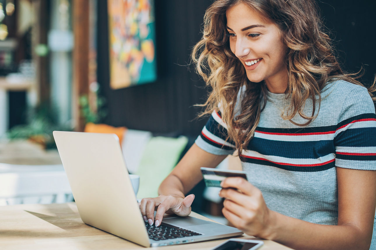 Junge Frau mit Karte in der Hand sitzt vor dem Computer